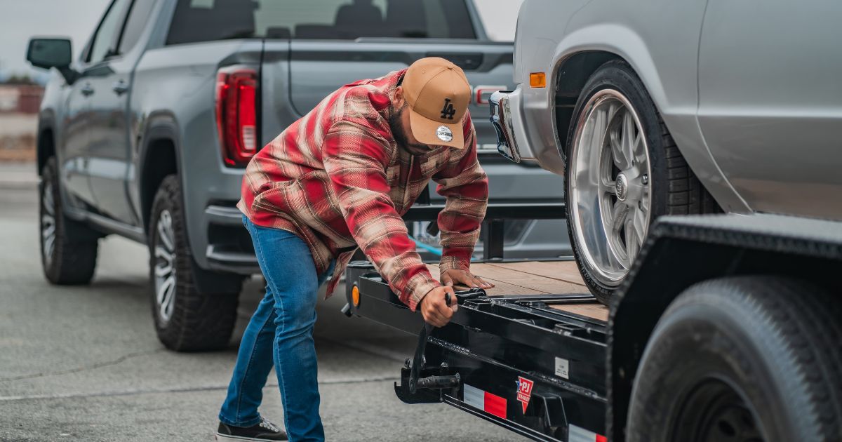 A man in a red and tan flannel is leaning over, performing trailer maintenance on his used trailer connected to a truck." width="1200" height="630