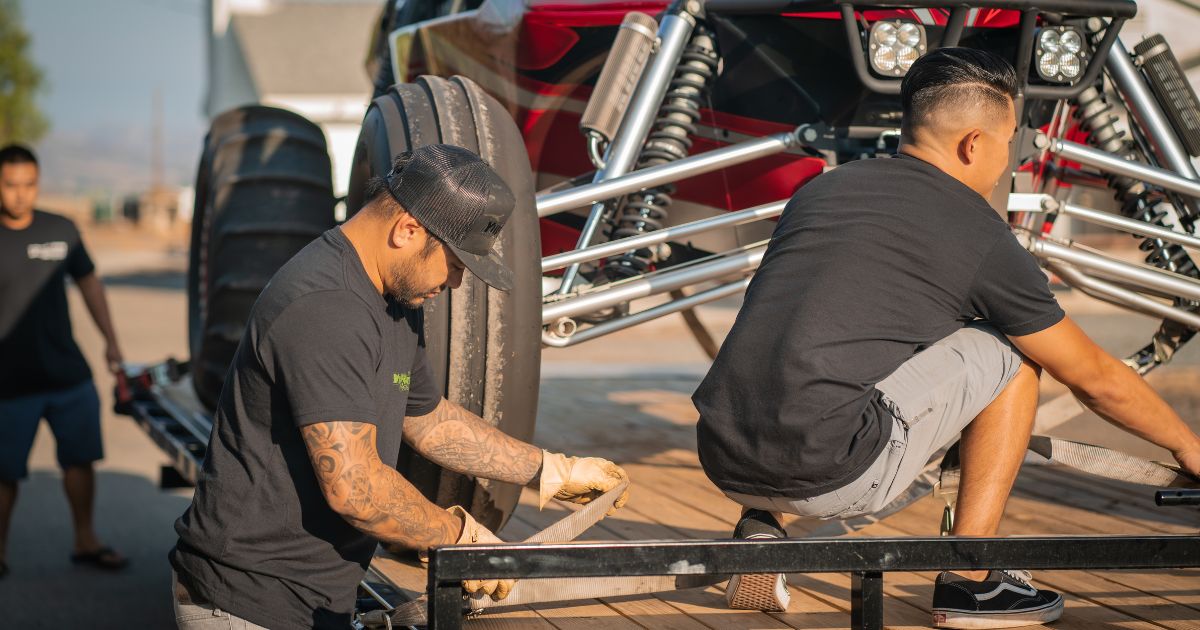 Men tying down a side by side to a new trailer that improves job site efficacy." width="1200" height="630